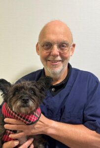 Dierenarts van Dierenkliniek Utrechtse Heuvelrug met een kleine hond in een geruit jasje op schoot